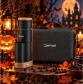 A Geimori portable coffee grinder set displayed on a rustic wooden surface with coffee beans, autumn leaves, a lantern, and a dark gray carrying case. The scene is styled in a Halloween-themed environment with a haunted house and full moon in the background.