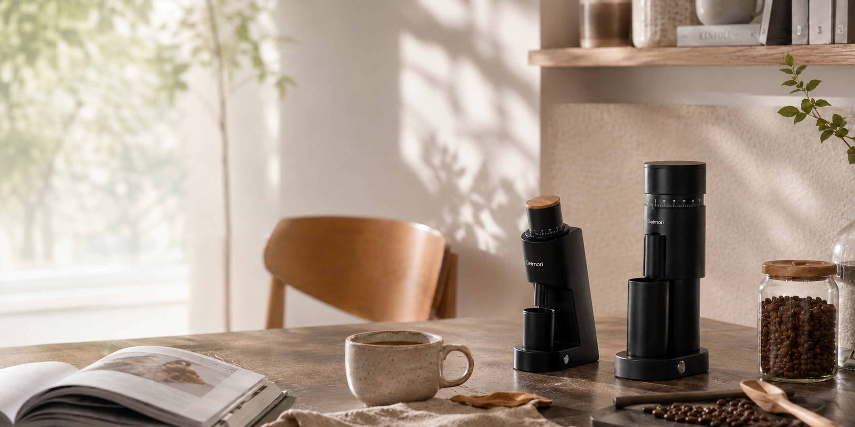A black manual coffee grinder and bean hopper set on a wooden table in a warm, sunlit kitchen setting with a coffee cup, beans, and an open book nearby.slider_item_3FJgtJ