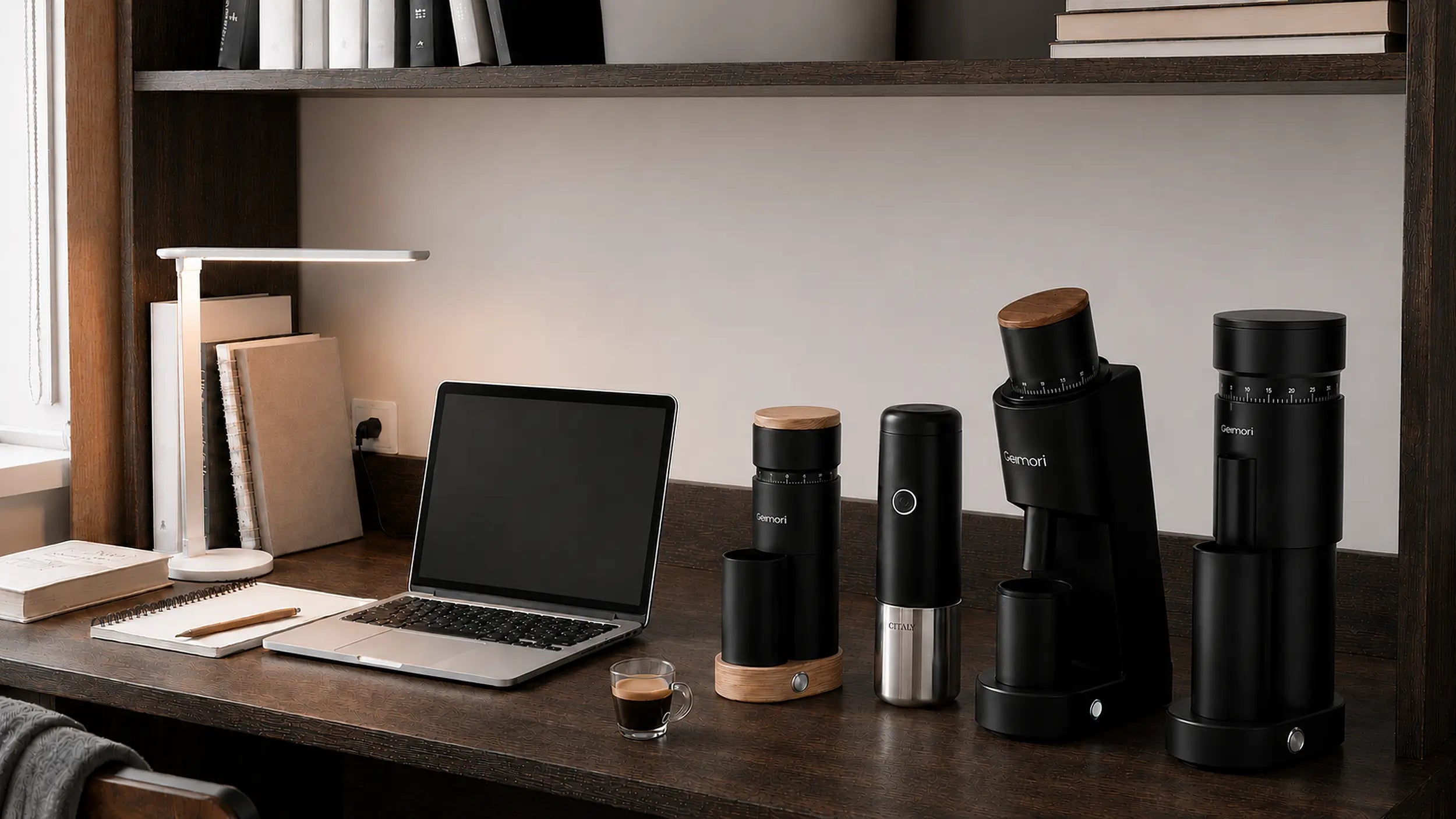 A set of black Mennip coffee brewing and grinding devices arranged on a wooden desk in a home office setting, alongside a laptop, lamp, and espresso cup.slider_item_TC6Wcc